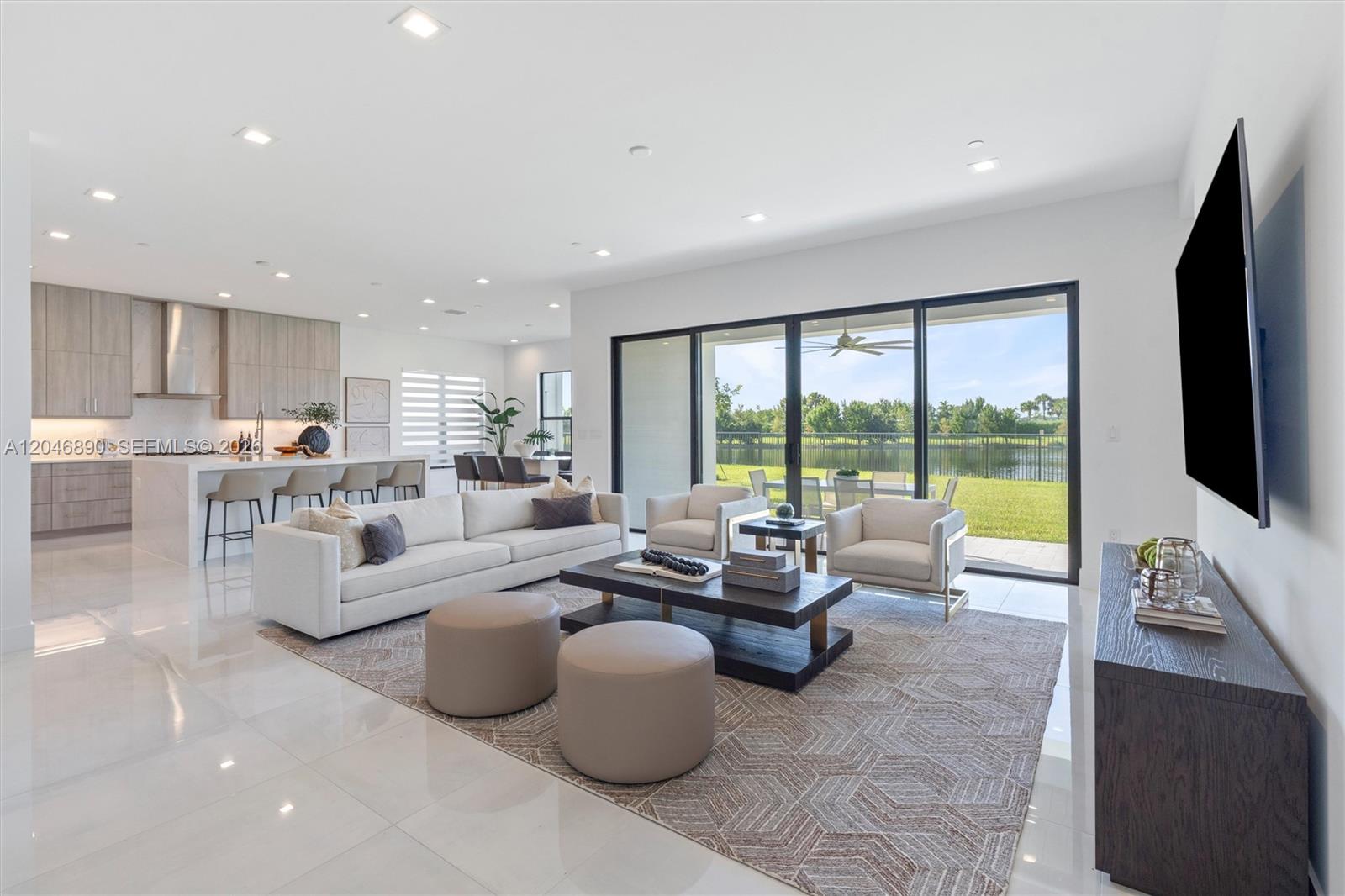 Staged open-plan living room with modern kitchen, sliding glass doors, and a lake view.
