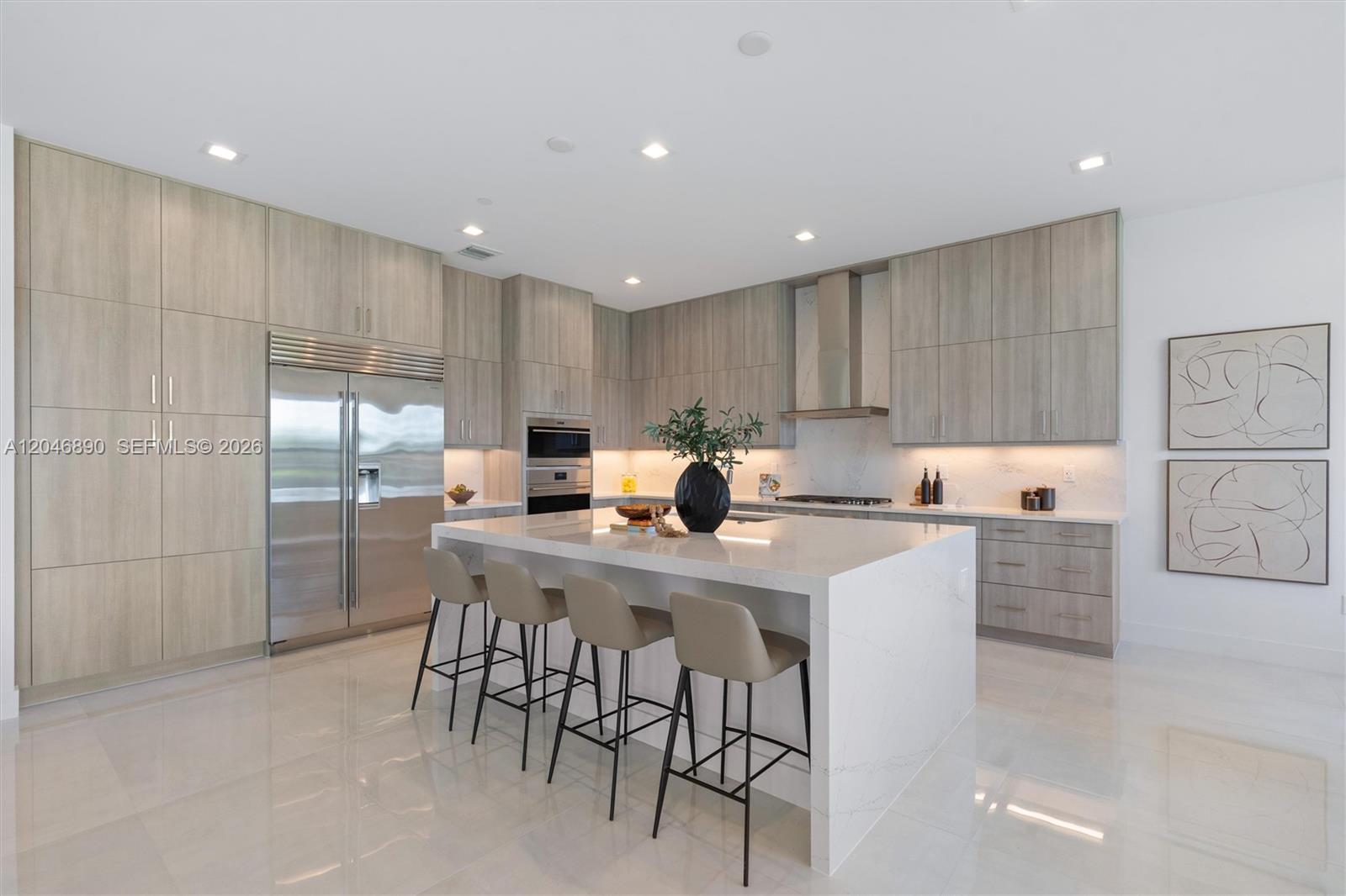 Modern kitchen with a large white waterfall island, light wood cabinets, and stainless steel appliances.