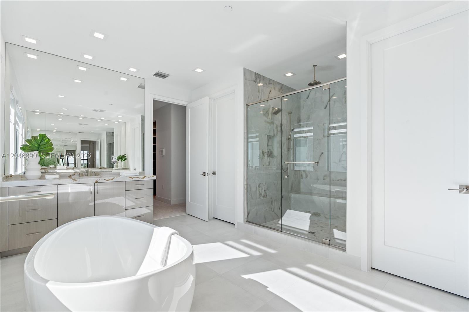 Bright bathroom with a freestanding soaking tub, double vanity, and marble-tiled glass shower.
