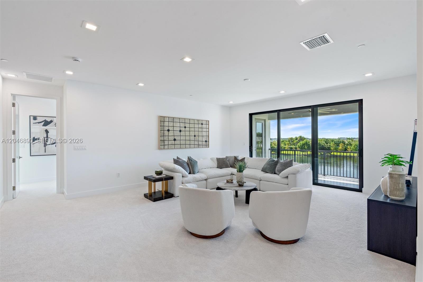 Furnished living room with a white sectional and balcony doors overlooking water and greenery.