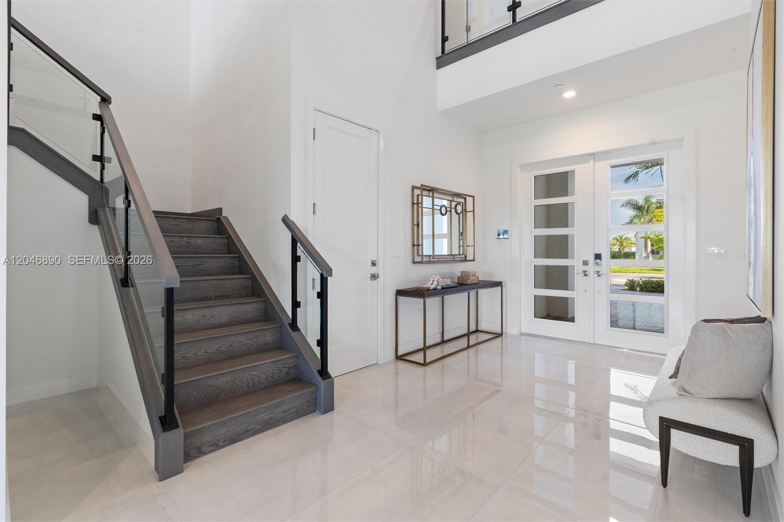 Entry foyer with a glass-railed staircase, glossy tile floors, and a glass-paneled front door.