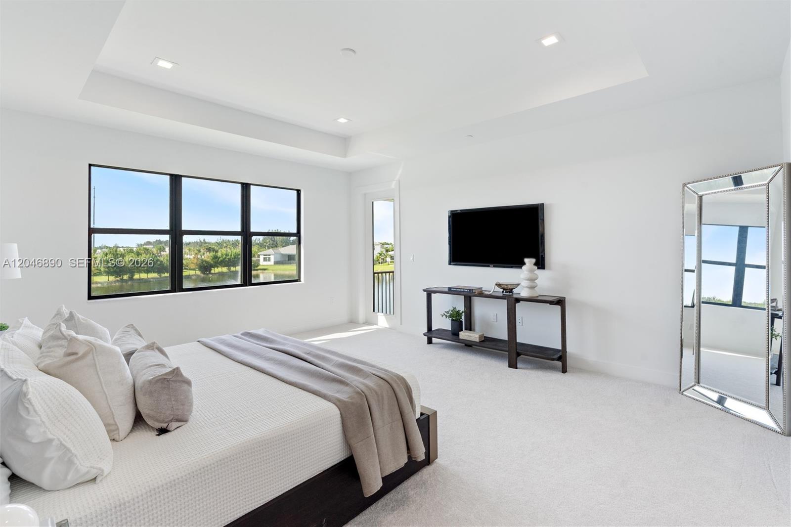 Furnished bedroom with large windows overlooking a pond and neighboring homes.