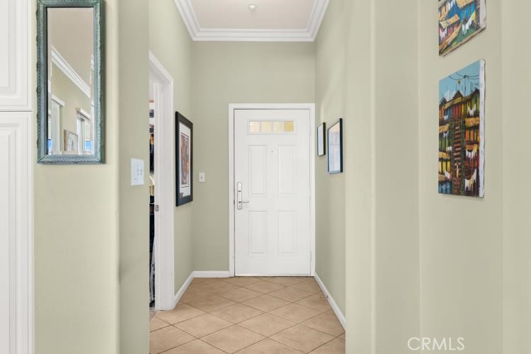 Entry hall with a white front door, beige tile floor, tall mirror, and framed artwork.