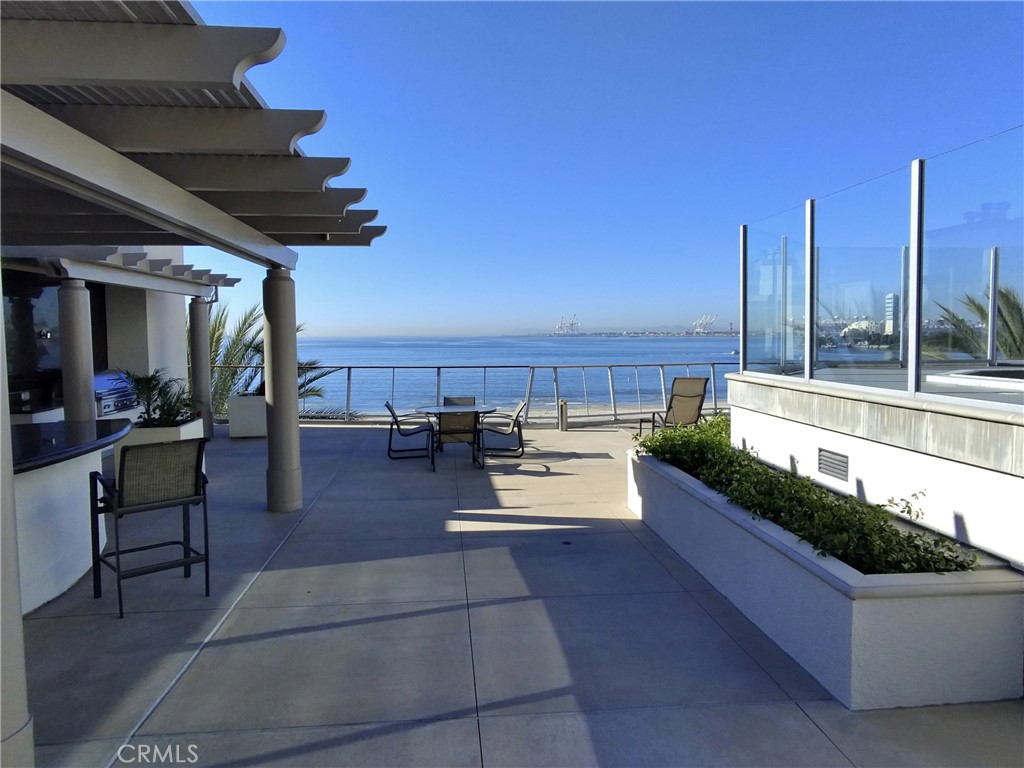 Oceanfront terrace with pergola, outdoor seating, glass wind screens, and distant waterfront views.