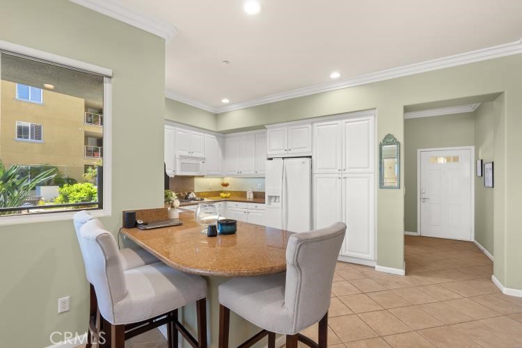 Kitchen with white cabinetry, granite breakfast bar, upholstered stools, and a large window overlooking greenery.