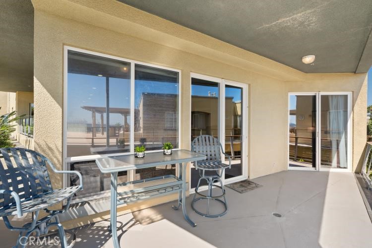 Covered balcony with a glass-top table, metal chairs, and sliding glass doors.
