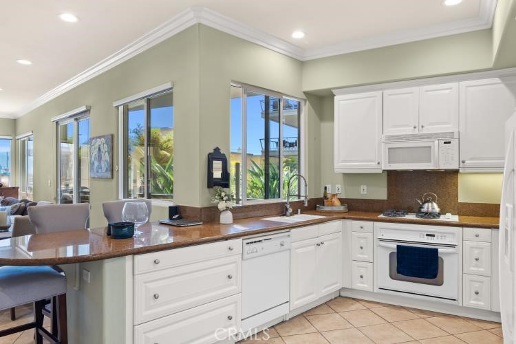 Condo kitchen with white cabinets, brown stone counters, and large windows beside the breakfast bar.