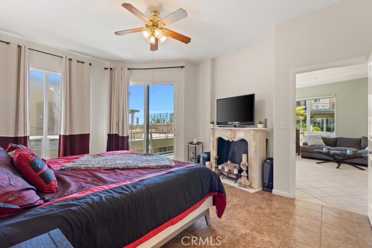 Bedroom with burgundy bedding, a ceiling fan, and a television above a fireplace.