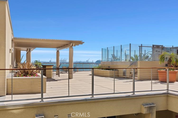 Rooftop terrace with pergola, glass railings, planters, and ocean views.