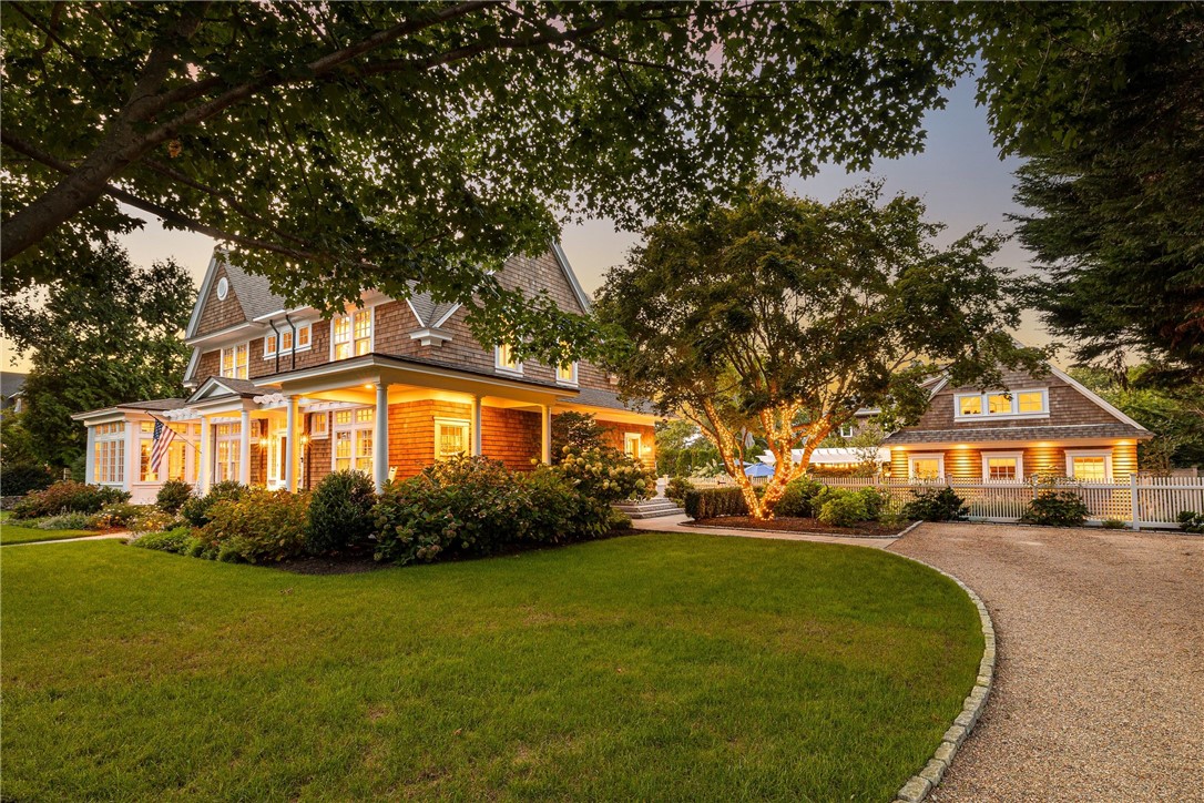 Shingle-sided home with a broad covered porch and detached garage at dusk.