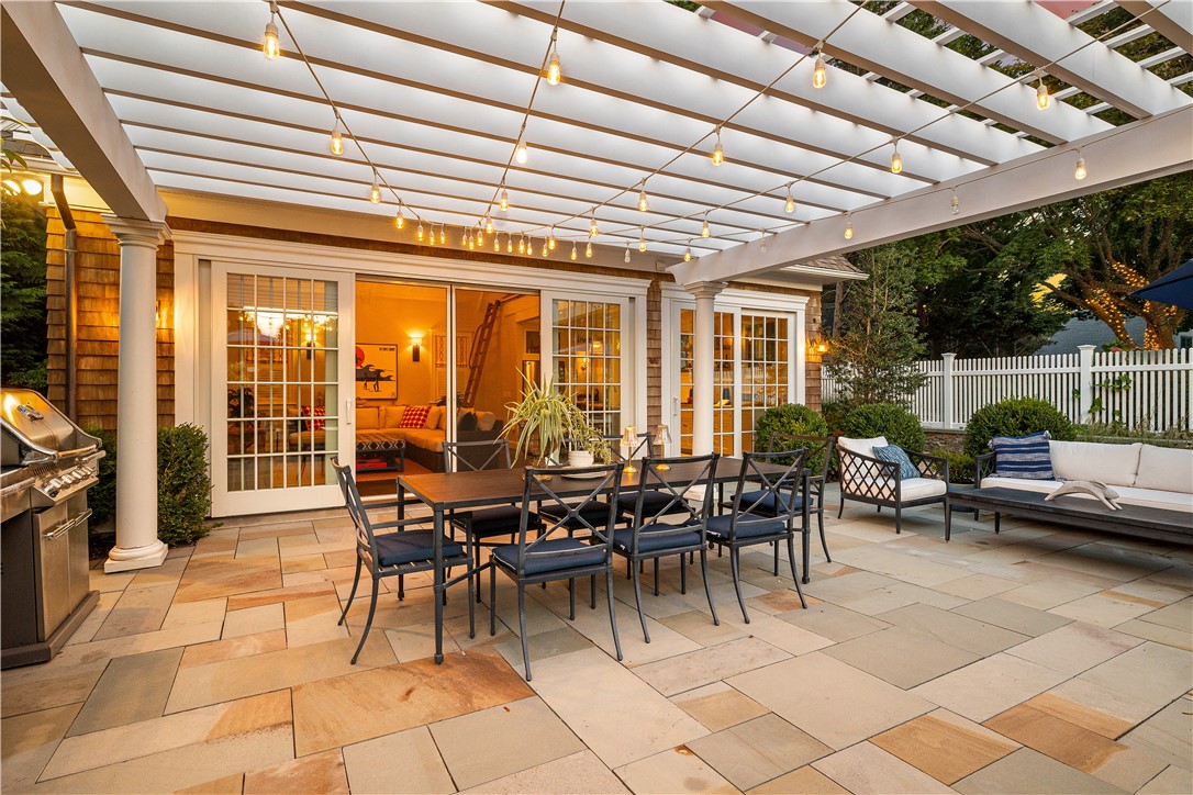 Stone patio beneath a light-strung pergola, with dining and lounge seating outside French doors.