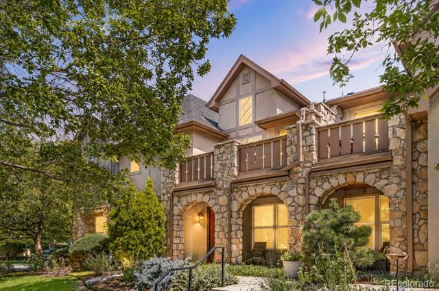 Two-story stone-and-timber home with a wooden balcony, framed by mature trees at dusk.