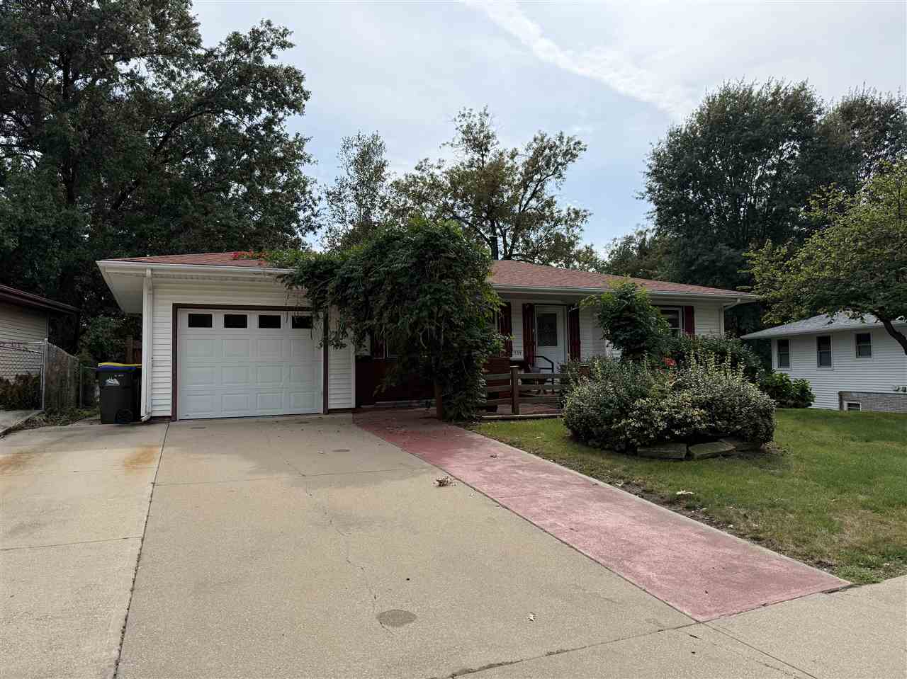 White ranch-style house with an attached garage, broad driveway, and tree-shaded front yard.
