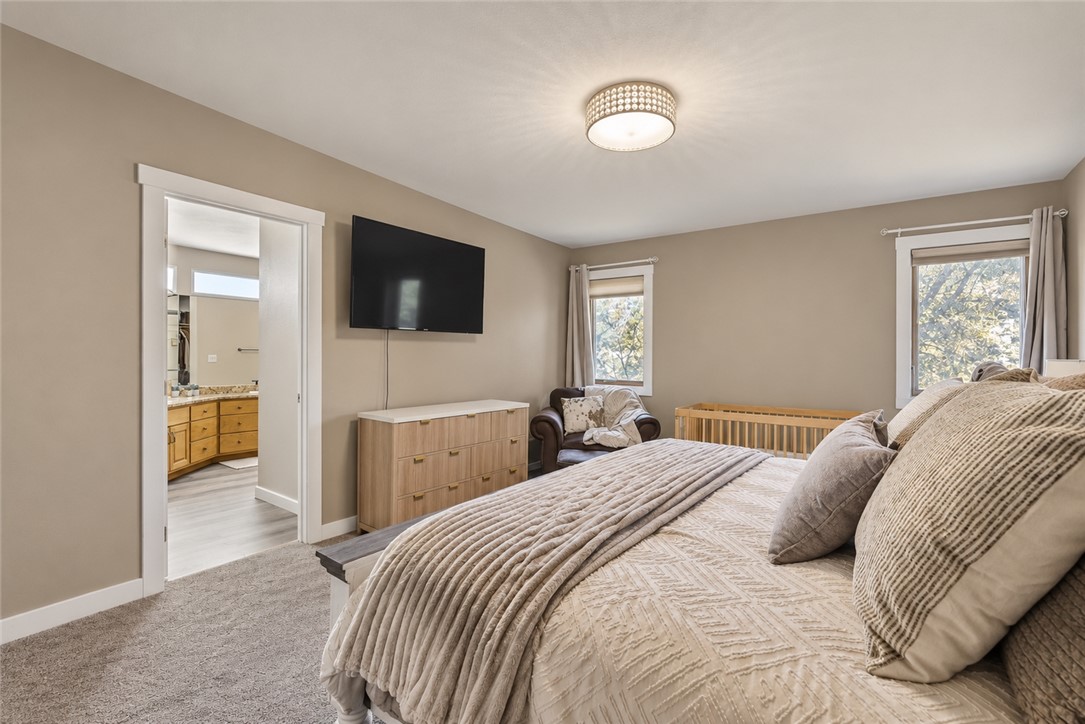 Bedroom with a beige quilted bed, wall-mounted television, and crib beside the windows.