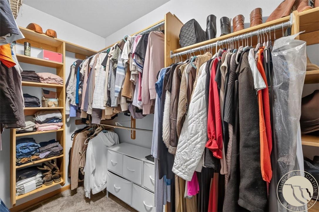 Walk-in closet with extensive clothing storage, wooden shelves, hanging garments, and white drawers.