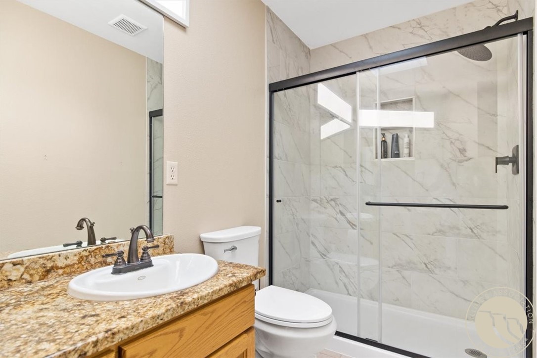 Bathroom with granite vanity and glass shower lined with marble-look tile.