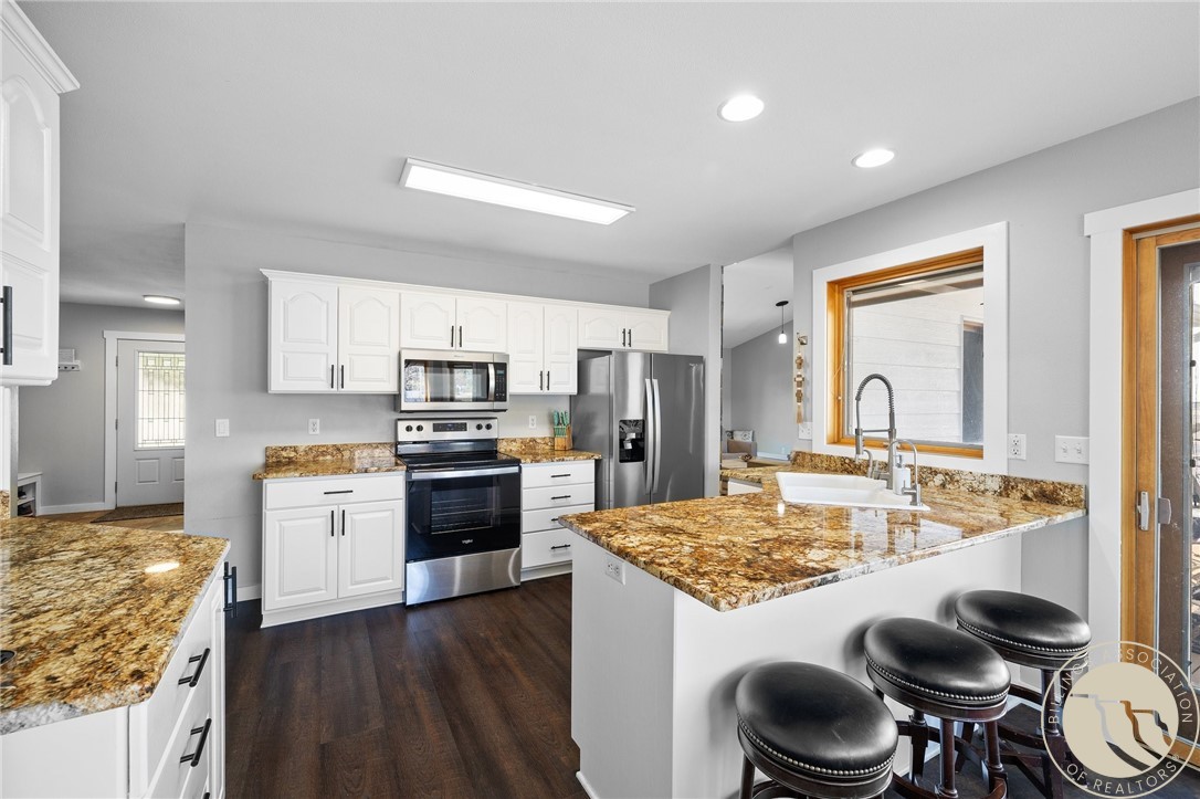 Kitchen with white cabinets, stainless steel appliances, patterned stone counters, and a large island with bar stools.