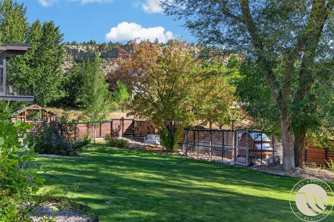 Backyard lawn with mature trees, wooden fencing, and rocky cliffs beyond.
