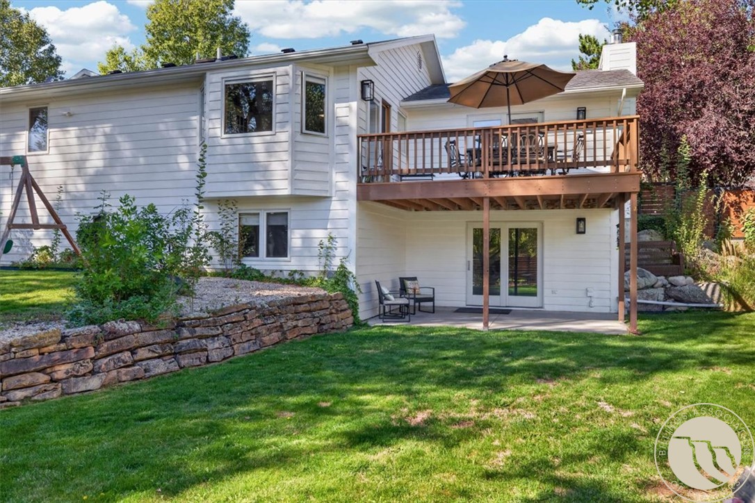 White home's rear exterior with a raised wooden deck and umbrella overlooking a green lawn.