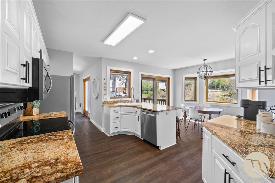Kitchen with white cabinets, granite counters, stainless steel appliances, and a dining area beside windows.