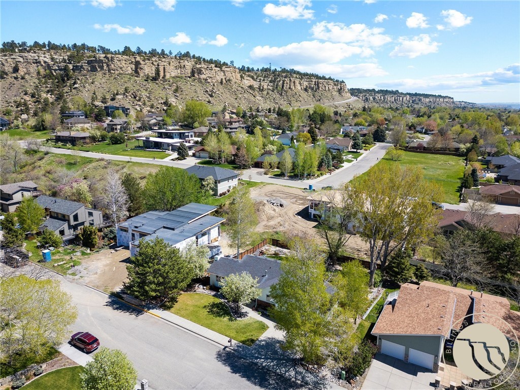 Aerial neighborhood view with a rocky cliff escarpment and a vacant lot among the homes.
