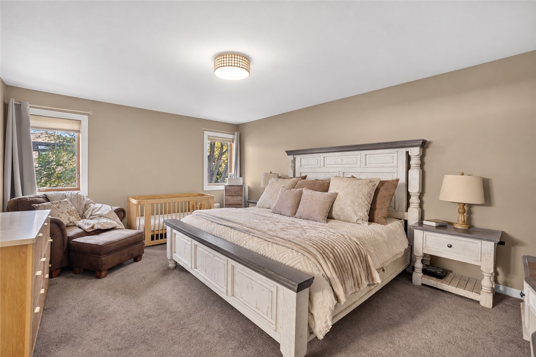 Bedroom with a large white bed, paneled headboard, wooden crib, and upholstered chair.