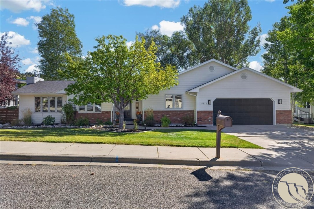 Single-story white and brick home with a dark two-car garage, leafy trees, and a front lawn.
