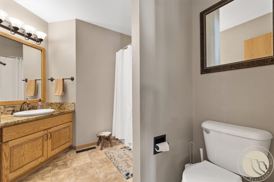 Bathroom with a wood vanity, granite countertop, tiled floor, and separate toilet area.