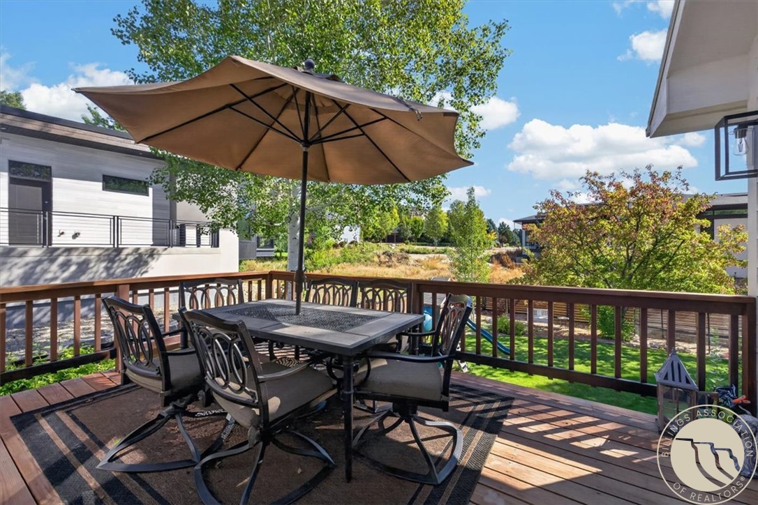 Deck patio with outdoor dining set and large umbrella overlooking landscaped grounds.