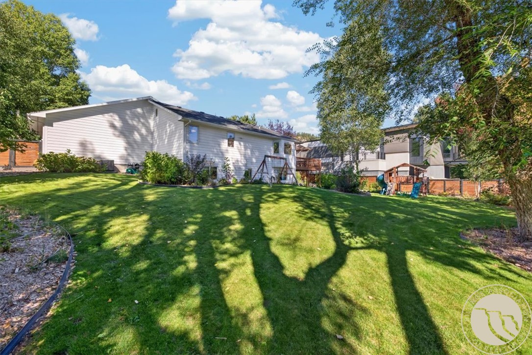 Rear of a single-story home beyond a broad lawn shaded by mature trees.