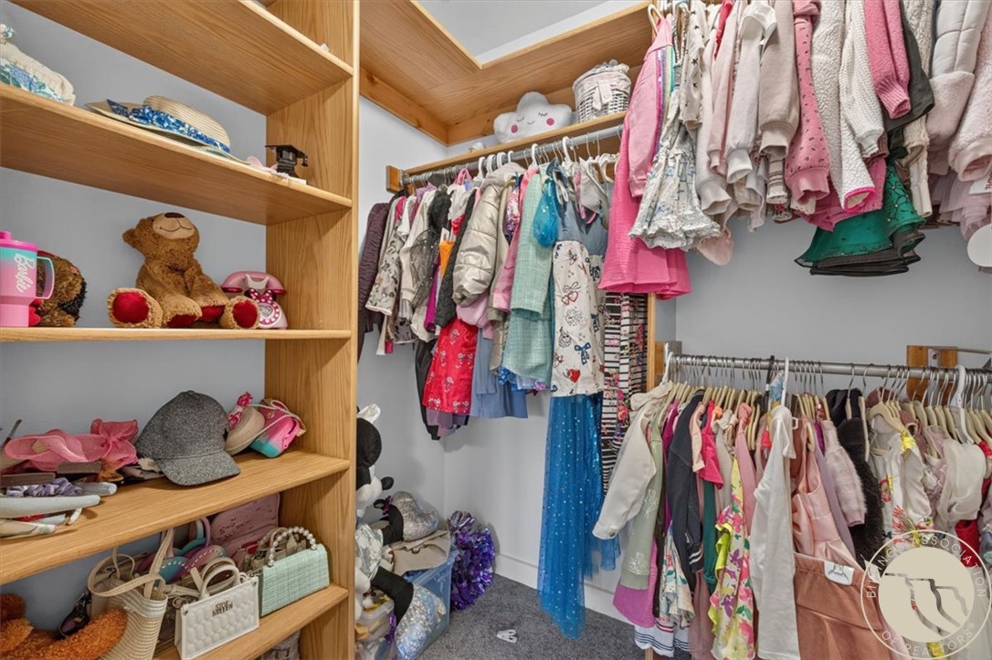 Walk-in closet with built-in wooden shelves and racks of children's clothing.