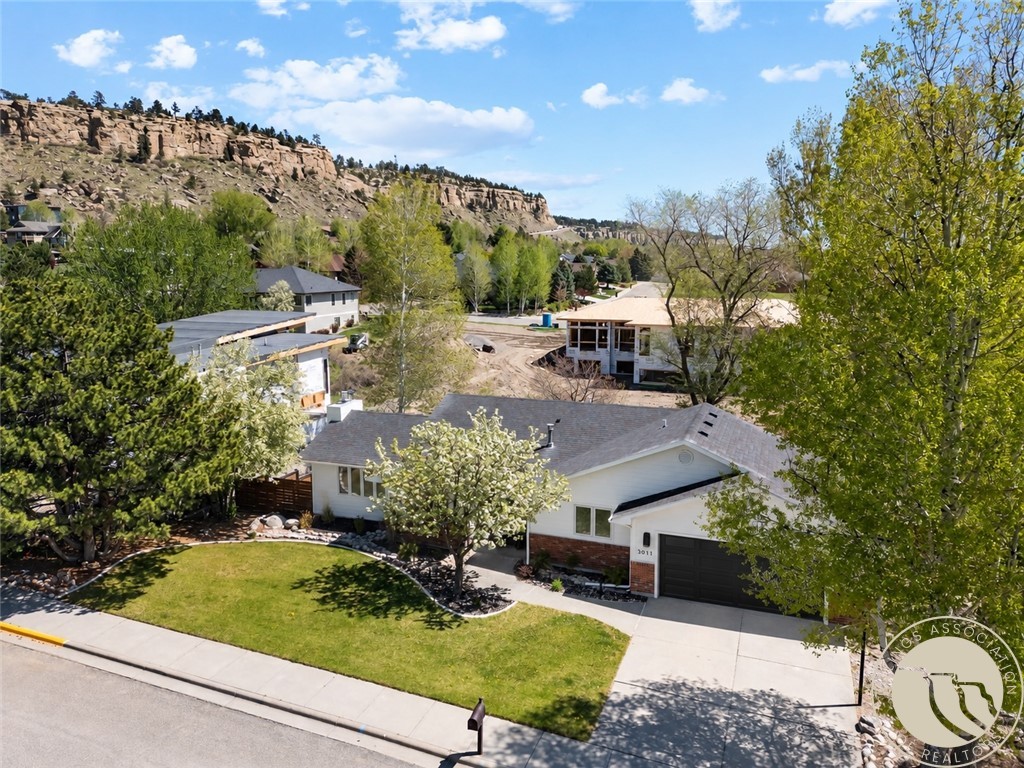 Single-story home with a dark garage door, landscaped lawn, and rocky ridge in the background.