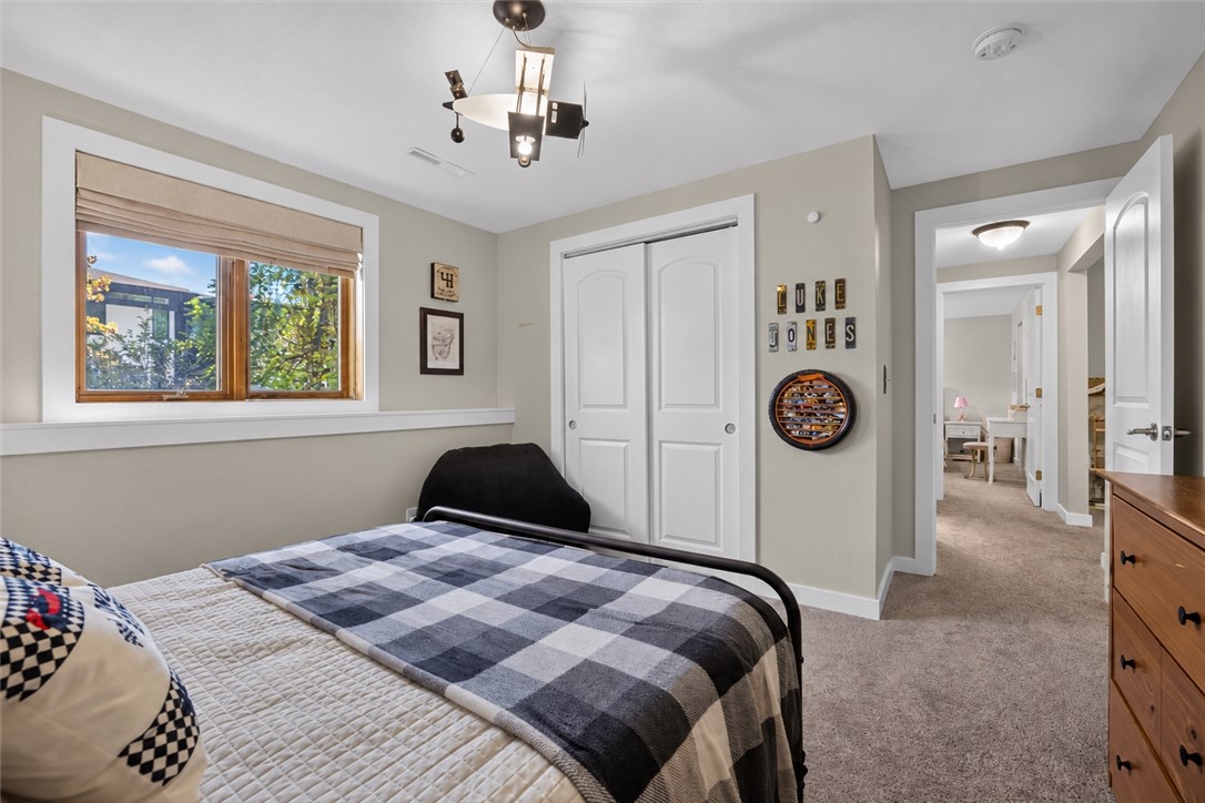 Bedroom with a blue-and-gray checked bedspread, large window, and white closet doors.