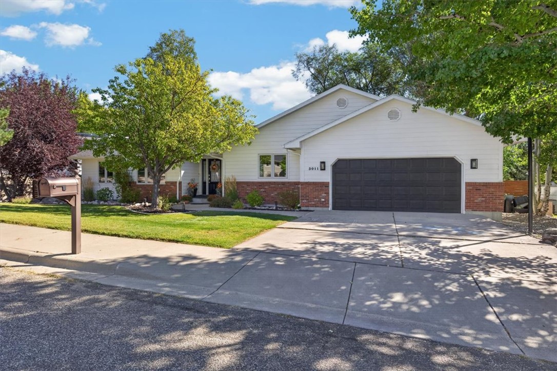 Single-story white home with brick facade, double garage, and mature trees.