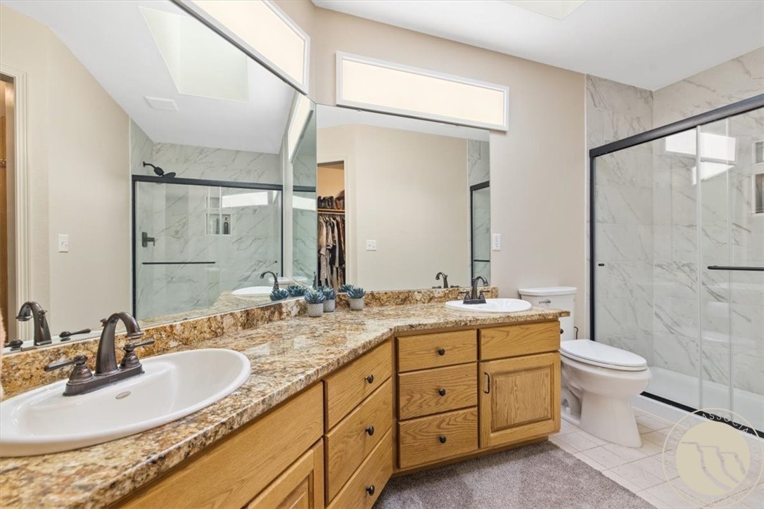 Bathroom with a double vanity, wood cabinets, stone countertop, and glass-enclosed tiled shower.