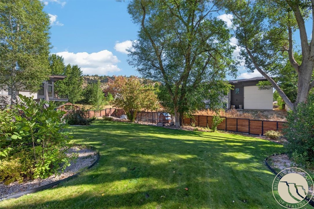 Backyard with a broad lawn, mature shade trees, and a wood-and-metal fence.