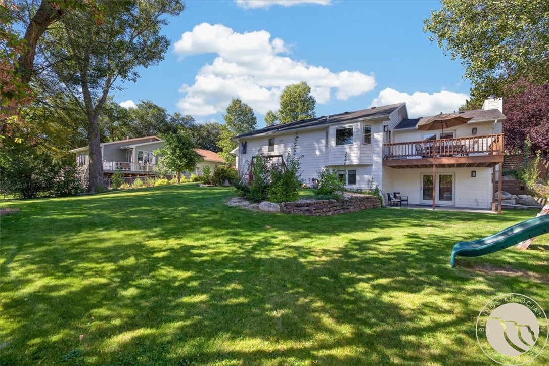 White two-level house with a raised deck overlooking a broad, tree-shaded lawn and garden.