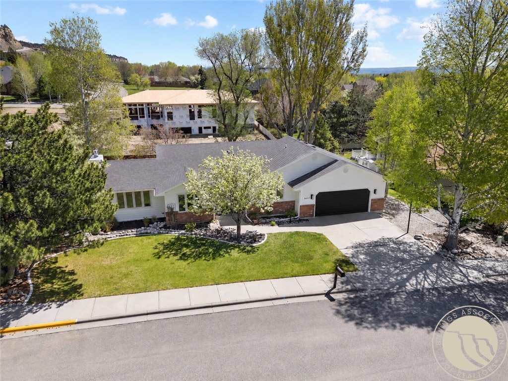 Aerial view of a single-story home with a two-car garage, green lawn, and mature trees.