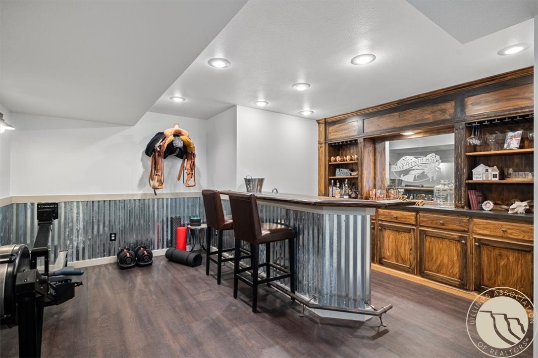 Basement bar with a corrugated-metal counter, leather stools, and a wood built-in back bar.