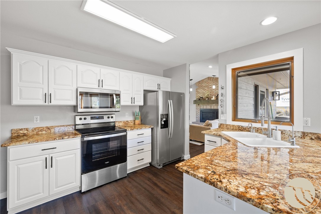 Kitchen with white cabinets, granite counters, stainless steel appliances, and a large island sink.