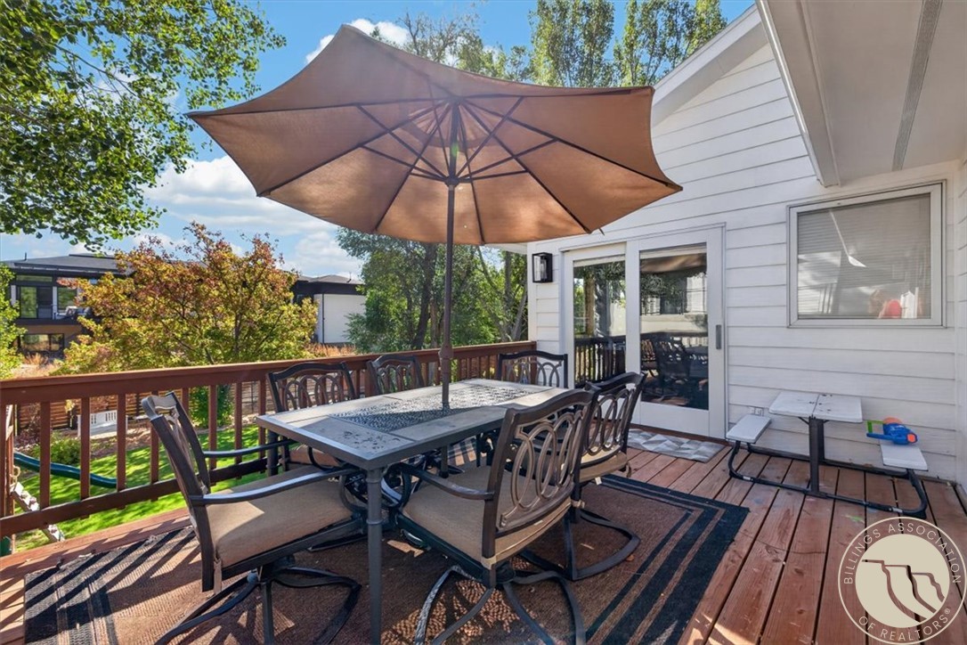 Deck dining area with a large brown umbrella, table and chairs overlooking a leafy yard.