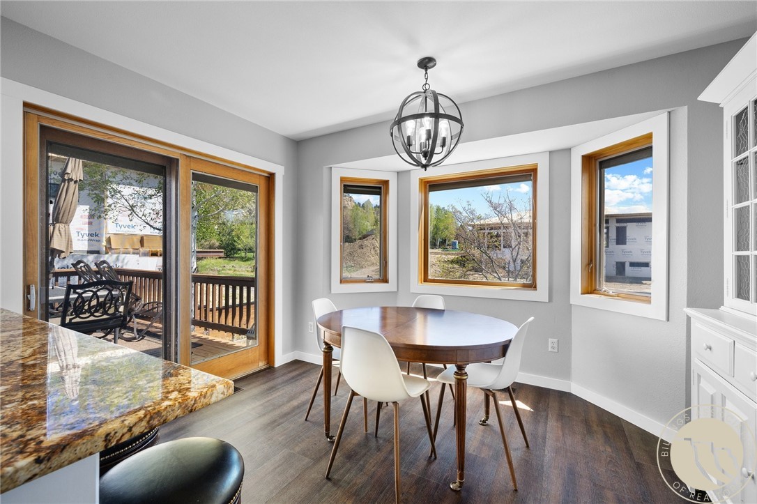 Dining area with a round wooden table, white chairs, and wood-trimmed windows overlooking a deck.