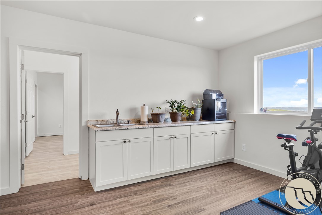 Bright room with white cabinets and a sink, exercise equipment, and a large window overlooking open land.