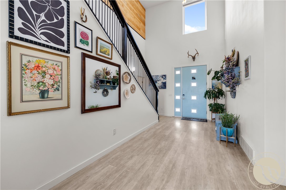 Entry foyer with a pale blue windowed front door, black-railed staircase, and framed floral artwork.