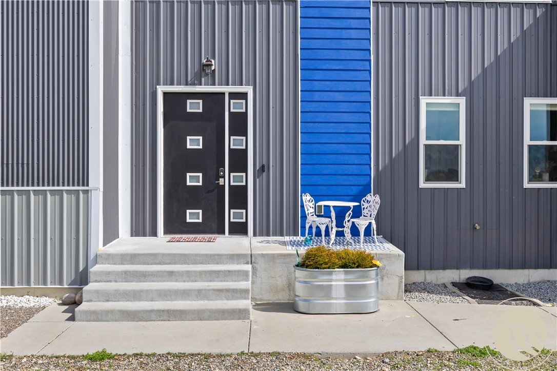 Modern building entrance with a black windowed door, blue accent wall, and white porch furniture.