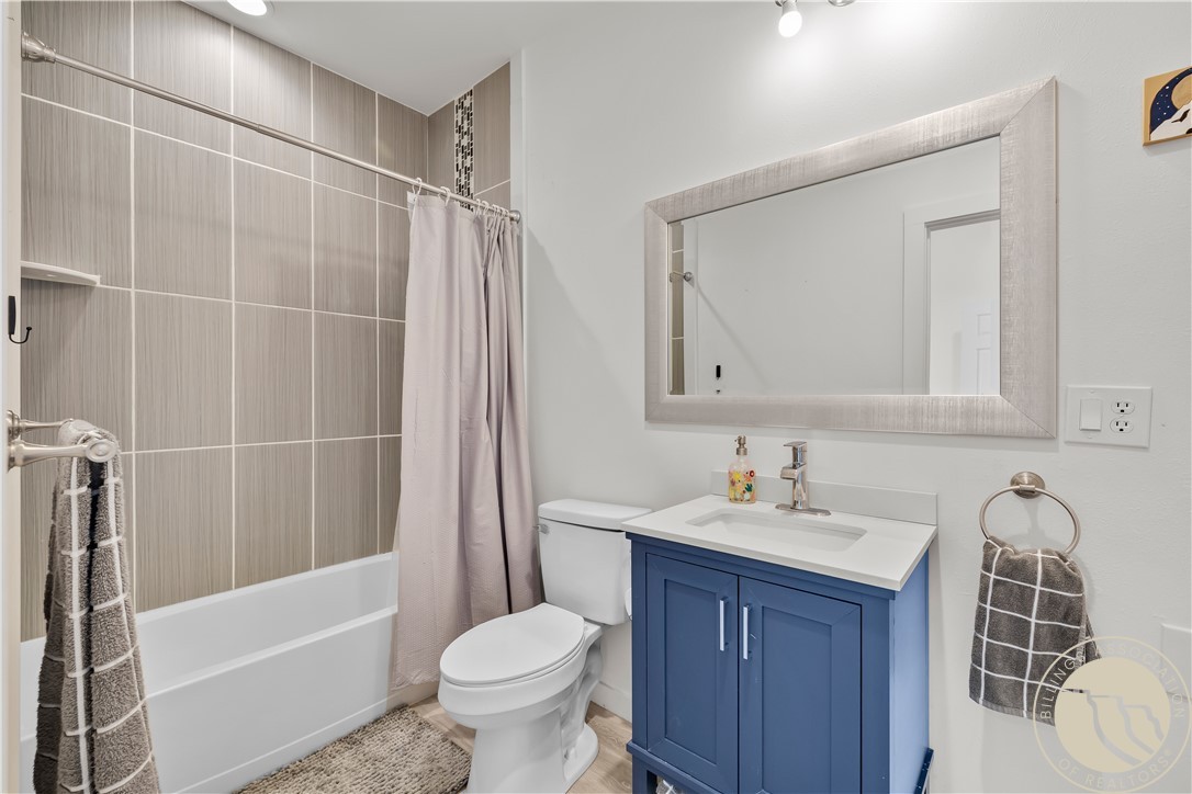 Bathroom with gray tiled tub surround, white shower curtain, and blue vanity.