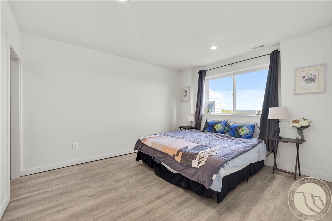 Furnished bedroom with a large bed beneath a wide window and dark curtains.