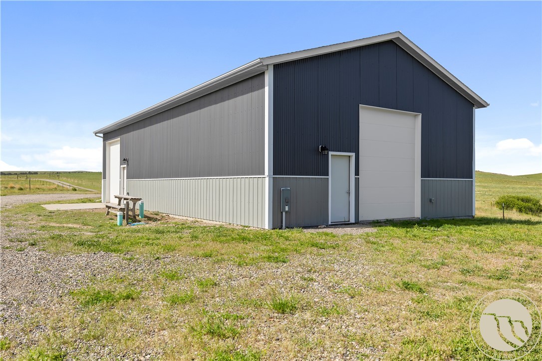 Gray metal outbuilding with a tall garage door on a grassy rural lot.