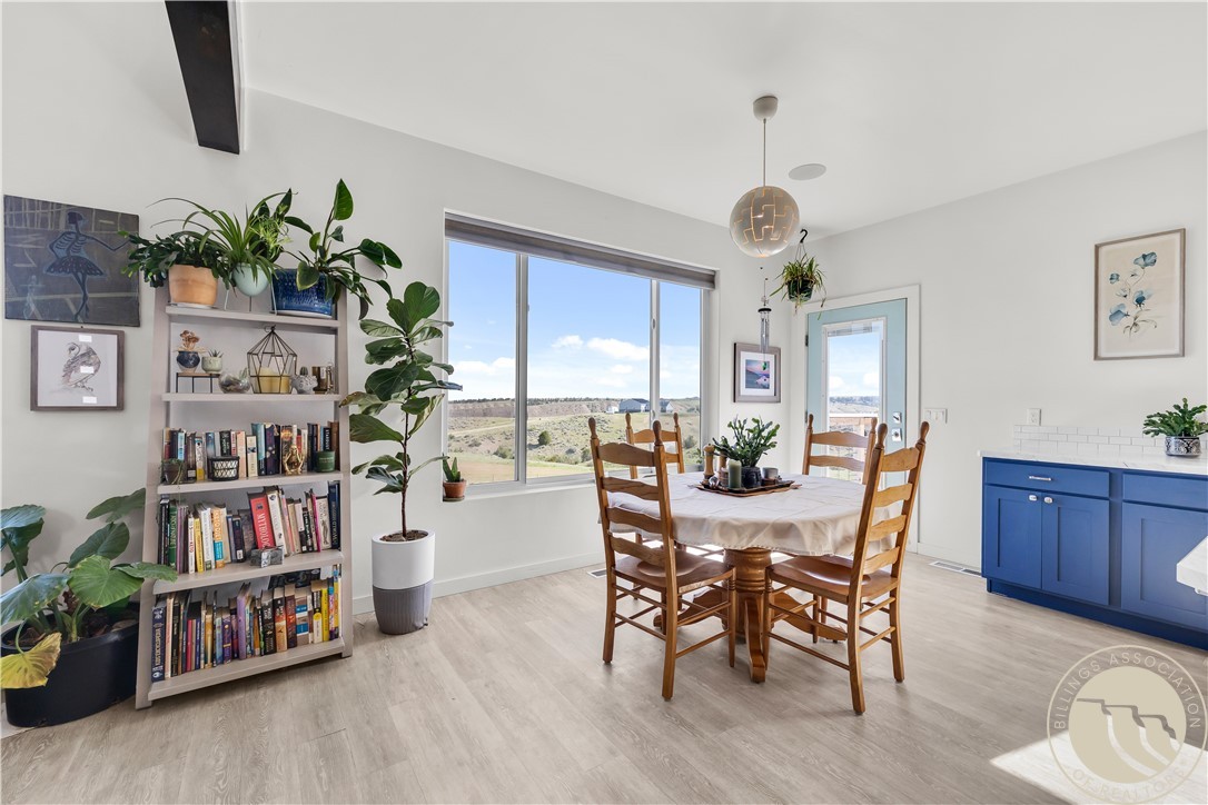 Dining area with a wooden table, blue cabinetry, and a large window overlooking rolling hills.