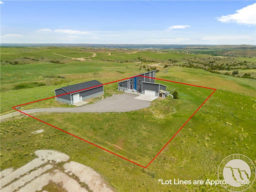 Aerial view of a gray home and detached outbuilding within red-marked lot lines on open rolling grassland.